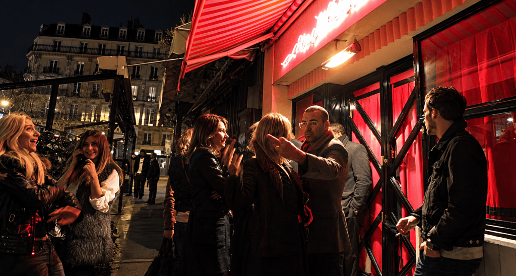 Pedestrians and fashionably dressed people on a Paris street during Fashion Week in the evening.